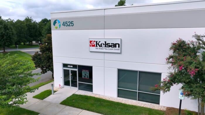 Exterior of a white commercial building with the address 4525 and a Kelsan sign above the entrance, surrounded by greenery and trees.