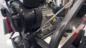 Close-up view of a portable pressure washer, showing its engine, control knob, metal frame, and hose connector.